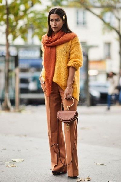 Желтый тонкий свитер оверсайз в сочетании с нюдовыми прямыми брюками-клеш, ботинками на каблуке и платформе, маленькой сумочкой и оранжевым шарфом.