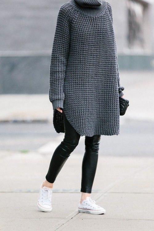 На девушке серый удлиненный свитер крупной вязки с разрезами по бокам, черные кожаные леггинсы, белые кеды и сумка-клатч.