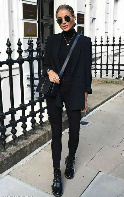 На девушки черный total look: водолазка с высоким горлом, джинсы скинни с завышенной талией, удлиненный пиджак прямого кроя, ботинки на шнуровке и с ремешками, поясная квадратная сумка, круглые очки и тонкая цепочка.
