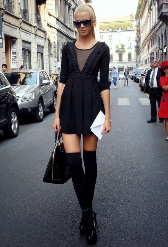 Черное платье-мини со свободной юбкой,черные теплые чулки и лаковые туфли на высоком каблуке и платформе. Образ дополняют квадратные очки и сумка.