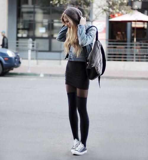 На девушке черная облегающая юбка-мини, джинсовая куртка, тонкие черные колготки, плотные чулки и кеды.