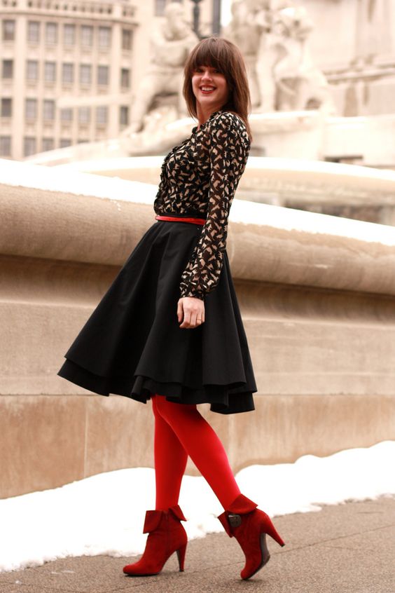На девушке черная рубашка, черная пышная юбка, красные чулки и темно-красные ботинки на каблуке.